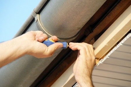 Contractor using a screwdriver to repair a brown rain gutter bracket