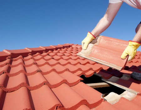 Fremont CA Tile Roof Repair and Installation Roofer in protective work gloves setting red Spanish clay tiles on a roof in Fremont CA