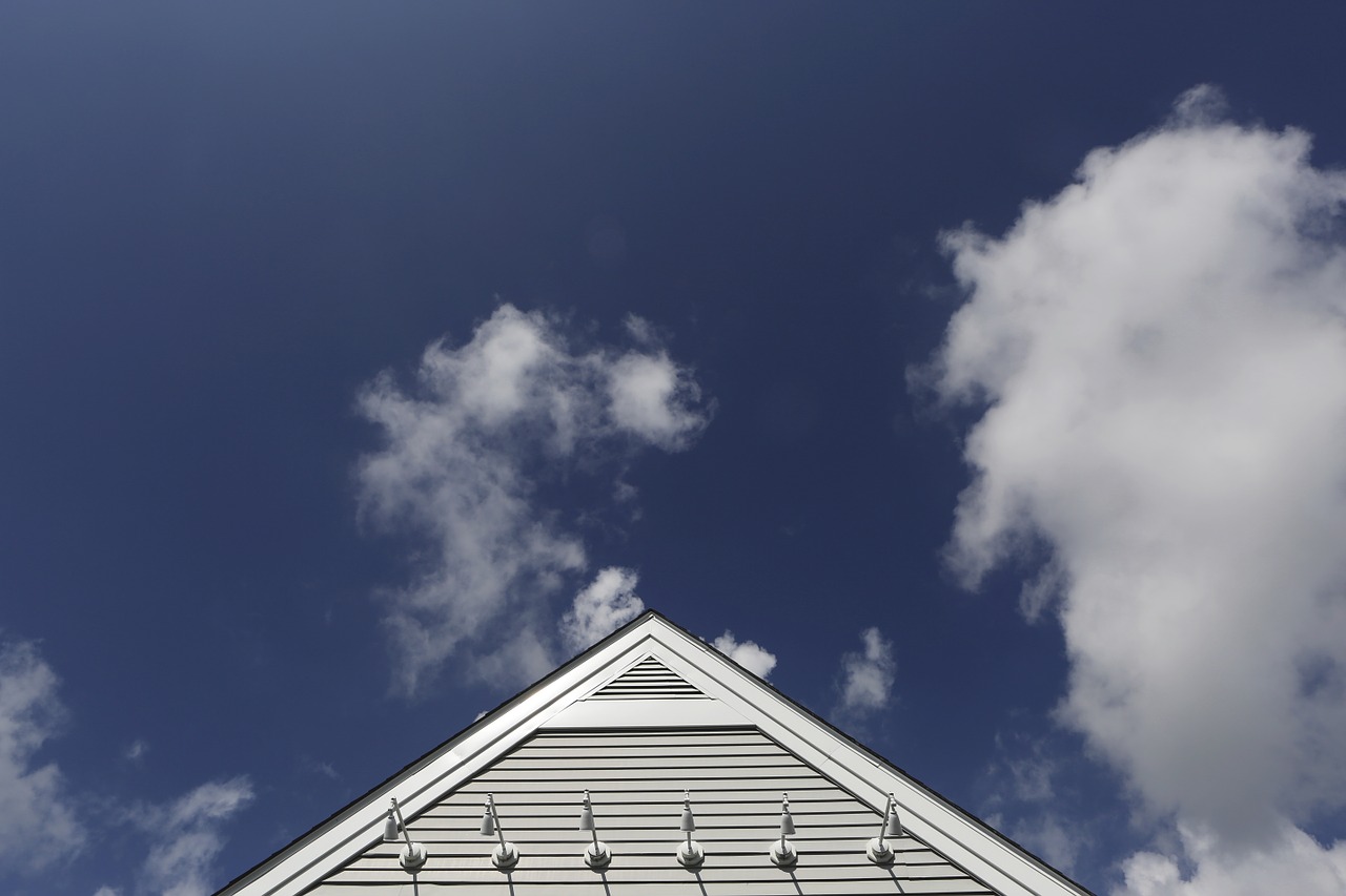 Triangular roof gable with white siding beneath a blue sky filled with white clouds.