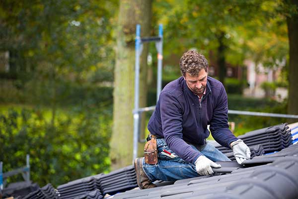 Roofer kneeling on dark gray roof tiles during a roof installation in Orinda CA