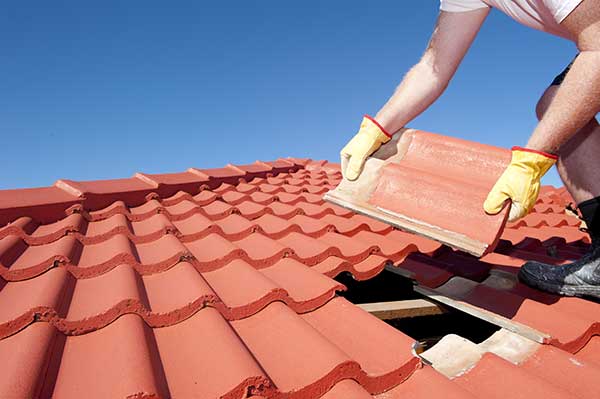 Roofer in yellow gloves laying red terracotta clay barrel roof tiles on a house in Orinda CA