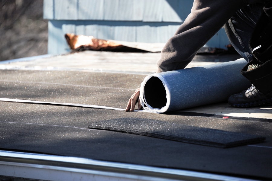 Roofing contractor unrolling black roofing membrane material on a flat commercial roof in Concord