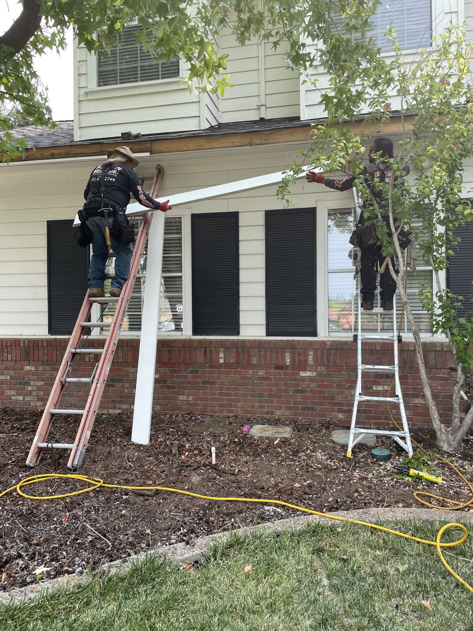 Residential Roof Repair and Exterior Maintenance Two roofing contractors on extension ladders working on the exterior trim and roofline of a two-story residential house